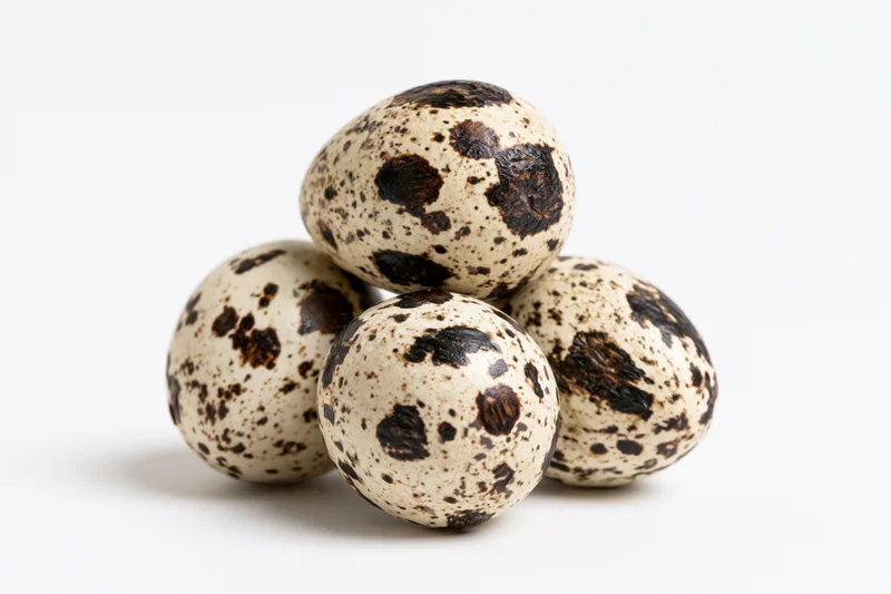Quail eggs arranged in a loose pyramid on a white surface