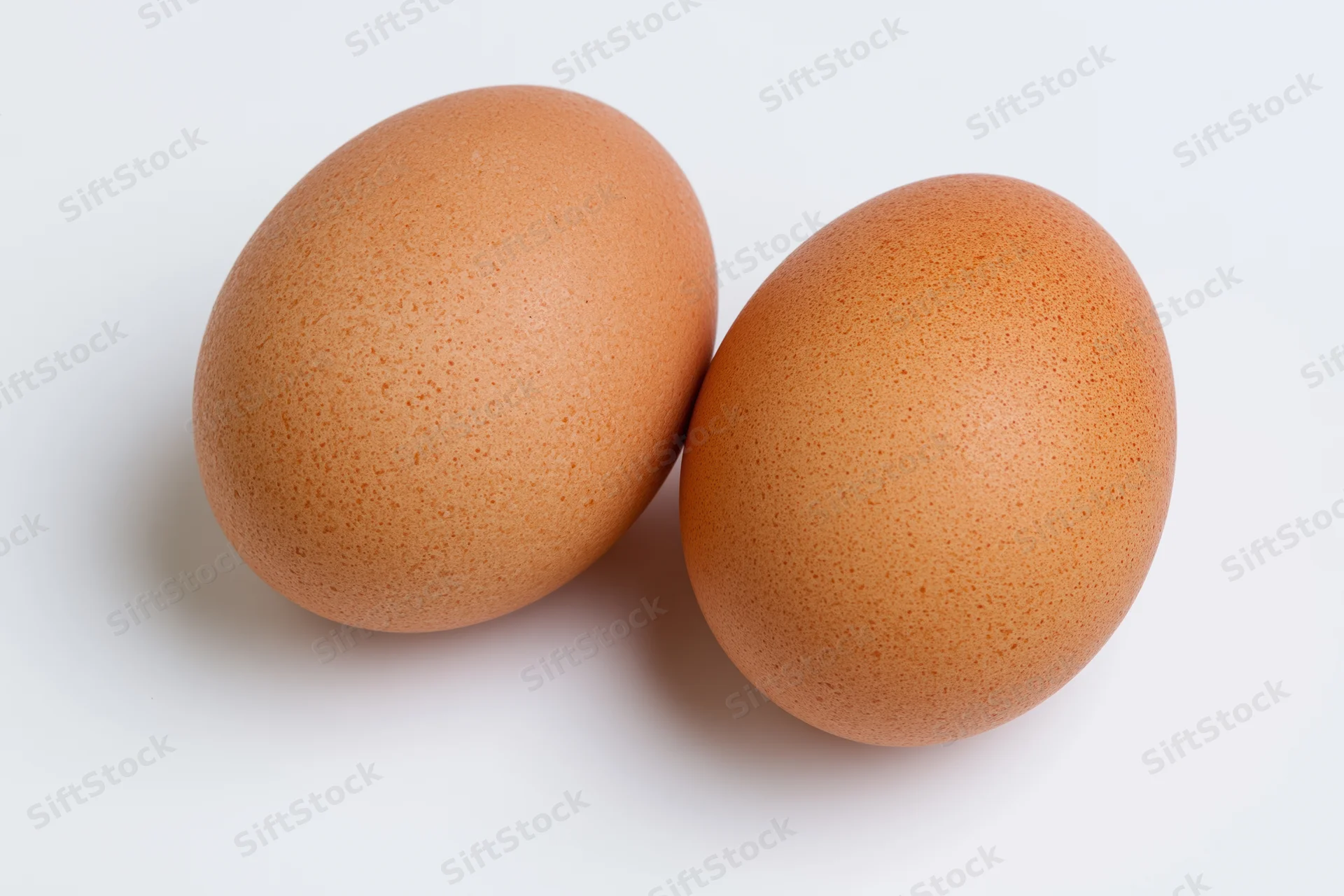 Two brown chicken eggs resting side by side on a plain white surface