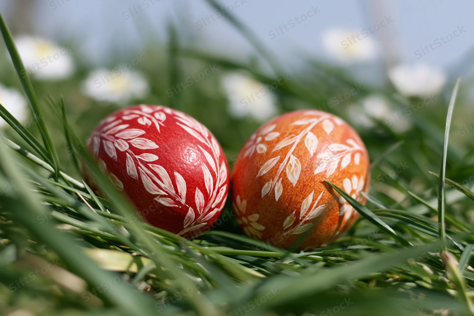Two hand-painted easter eggs with white floral patterns resting in green grass