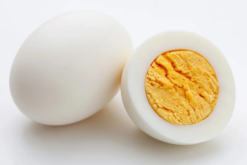Two hard-boiled eggs one whole and one halved on a white background