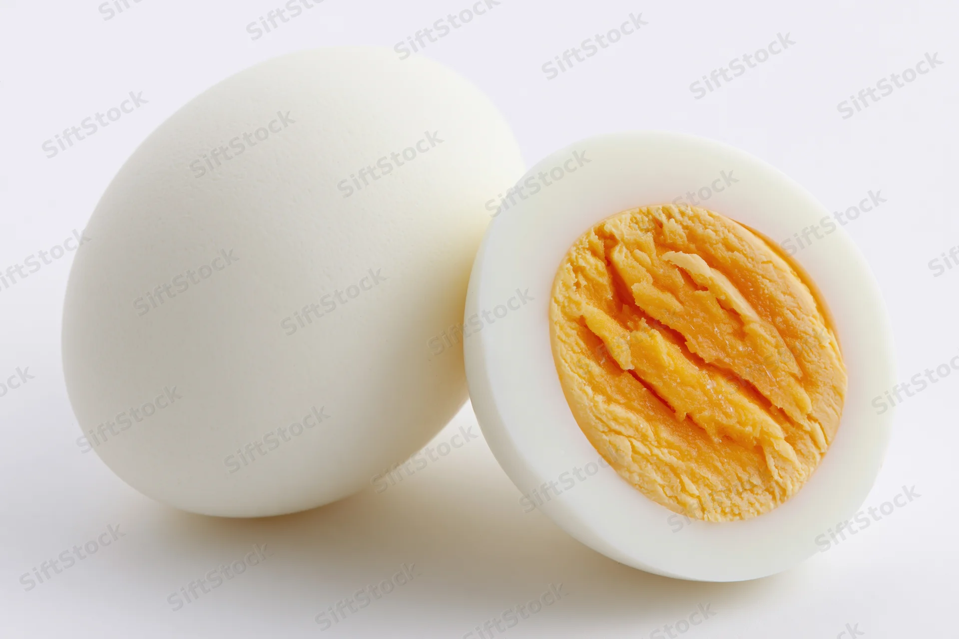 Two hard-boiled eggs one whole and one halved on a white background