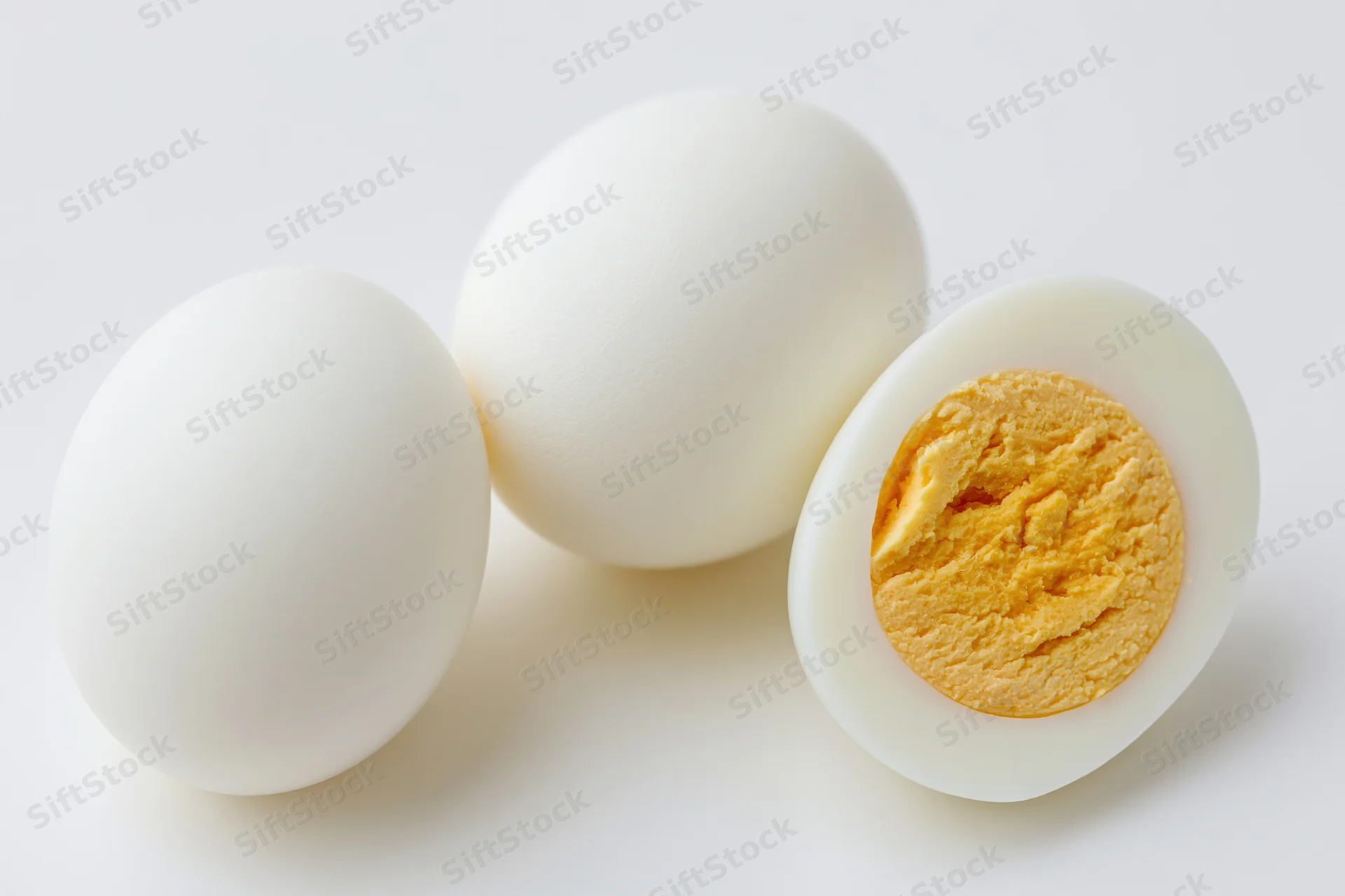 Two hard-boiled eggs on white background one whole and one halved showing yolk