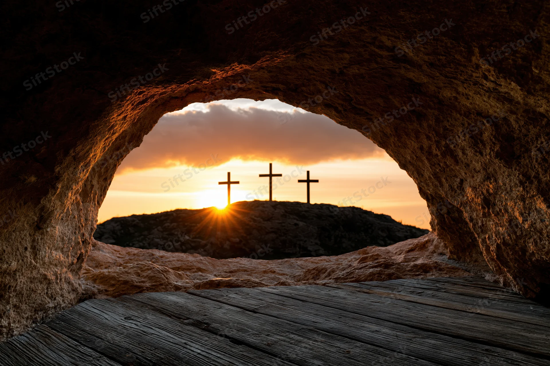View from inside a stone cave looking out at three crosses on a hill at sunset