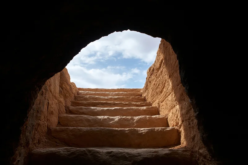 Stone staircase leading upward from dark cave entrance to bright sky in desert ruin