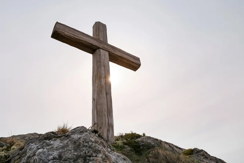 Weathered wooden cross standing on rocky hilltop with sun behind it