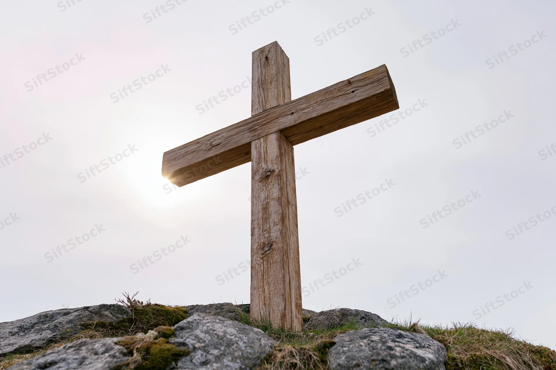 Weathered wooden cross standing on rocky hilltop under bright sky