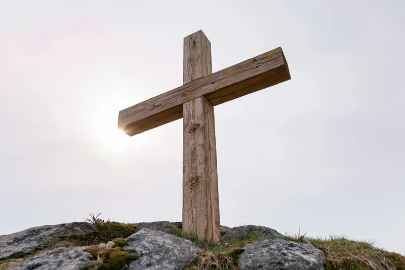 Weathered wooden cross standing on rocky hilltop under bright sky