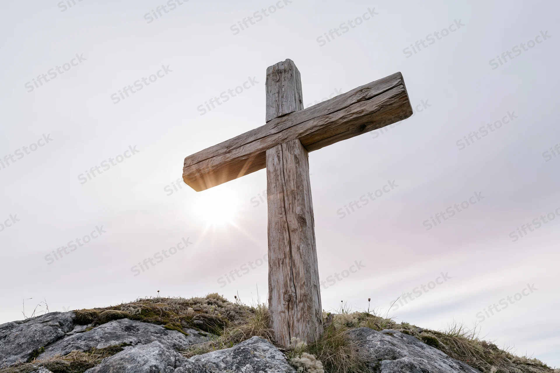 Weathered wooden cross standing on rocky hilltop under bright sunlit sky
