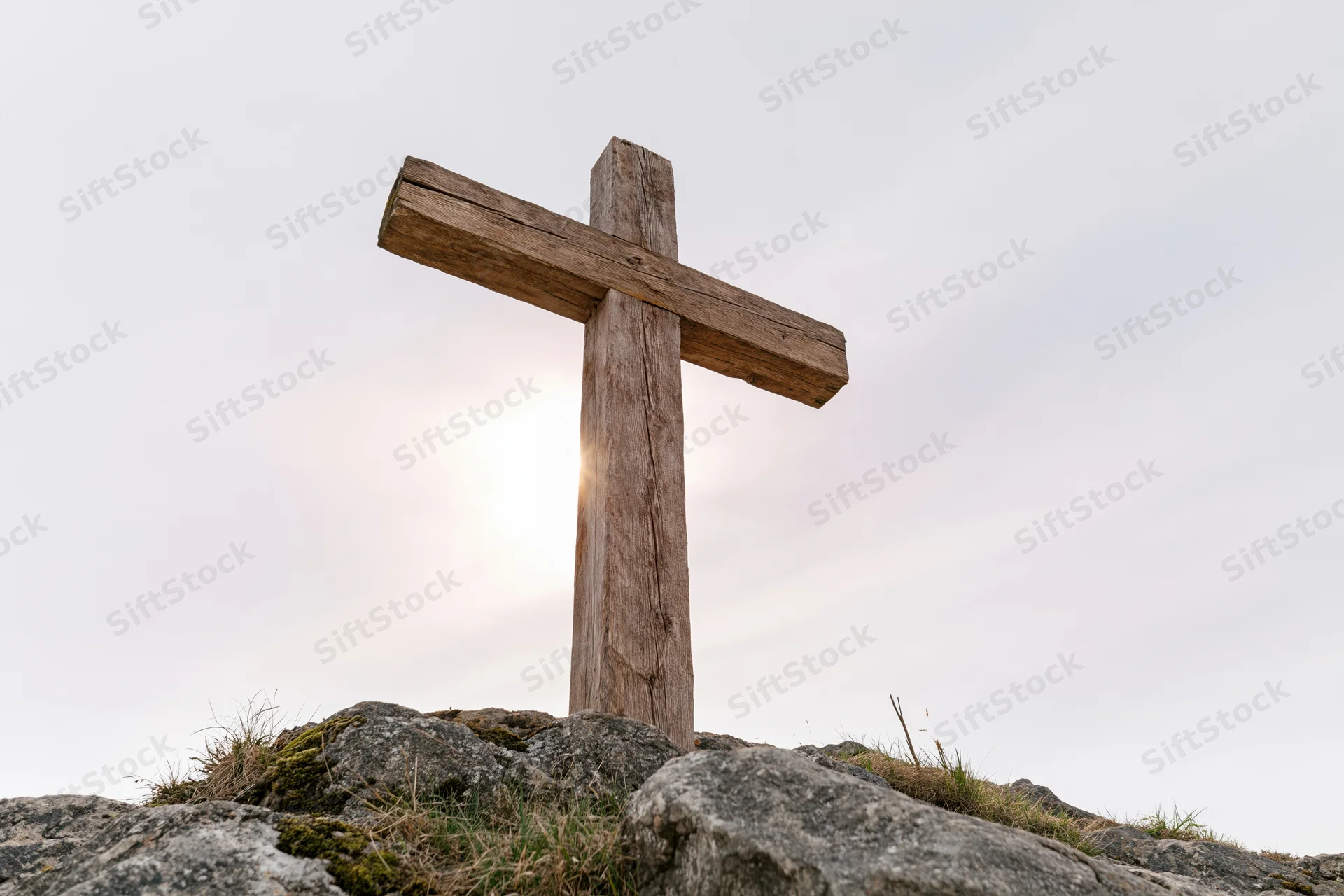 Weathered wooden cross standing on rocky hilltop under bright sky