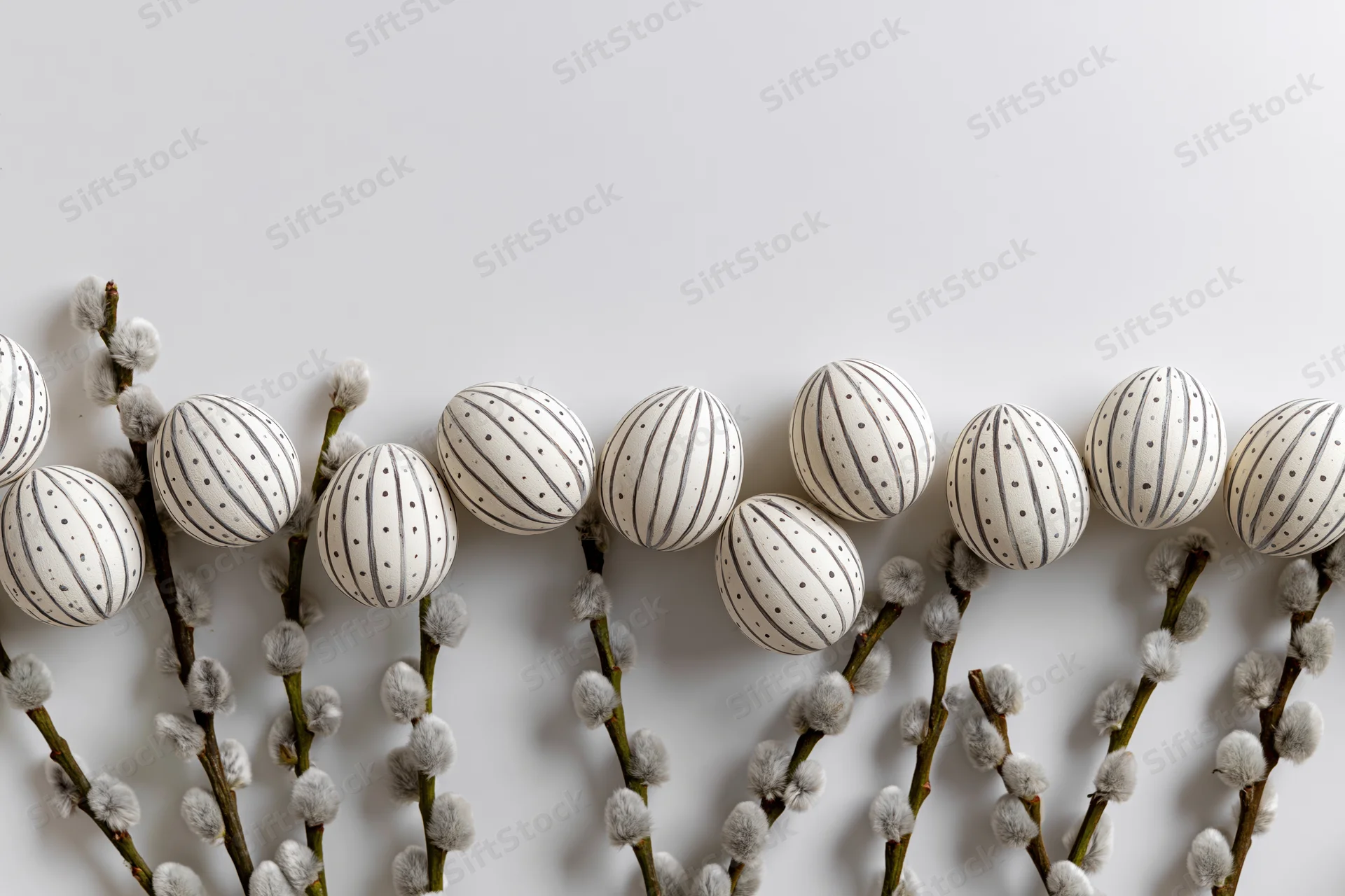 White decorated easter eggs with stripes and dots arranged on willow branches with catkins in a flat lay composition