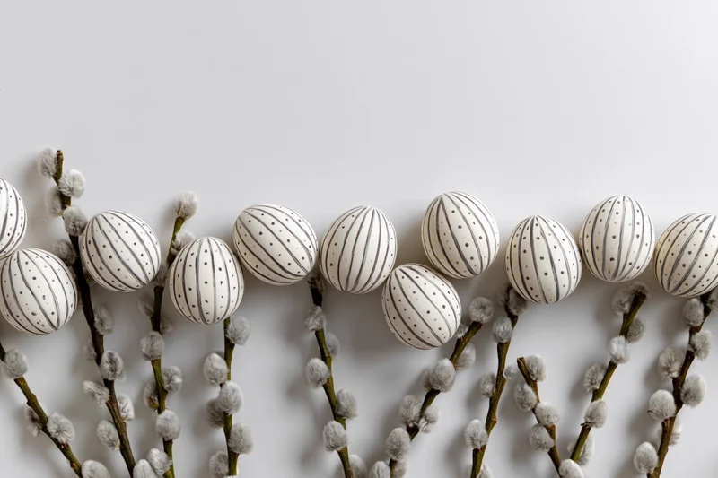 White decorated easter eggs with stripes and dots arranged on willow branches with catkins in a flat lay composition