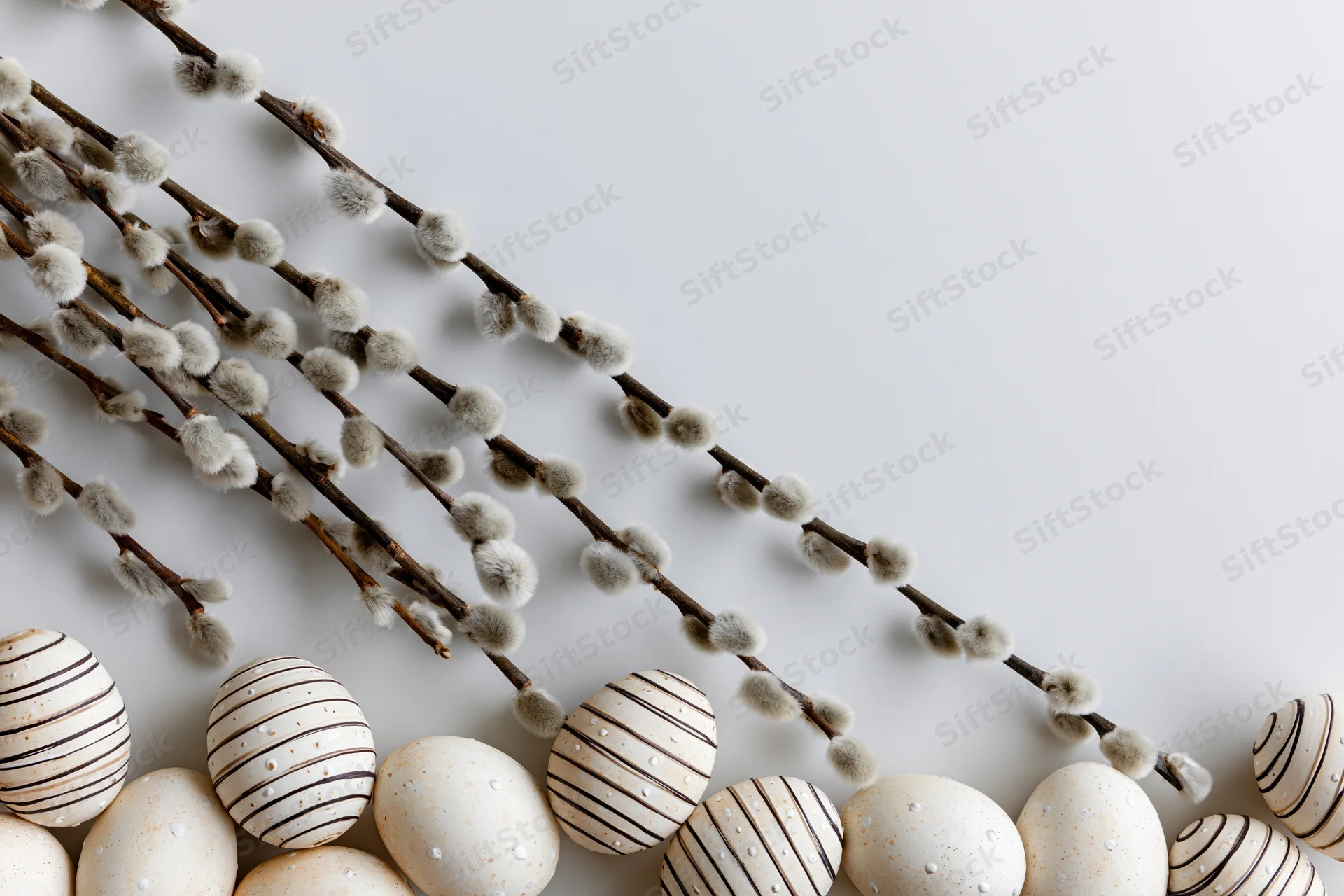 White striped Easter eggs and willow branches arranged on a plain surface with copyspace