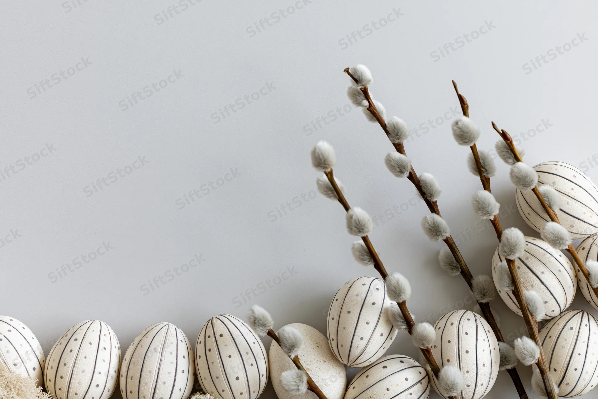 White striped easter eggs and willow branches arranged in a flat lay on a light gray surface