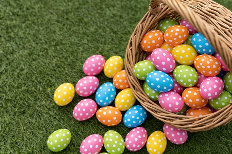 Wicker basket tipped over with colorful polka-dotted easter eggs spilling onto green grass