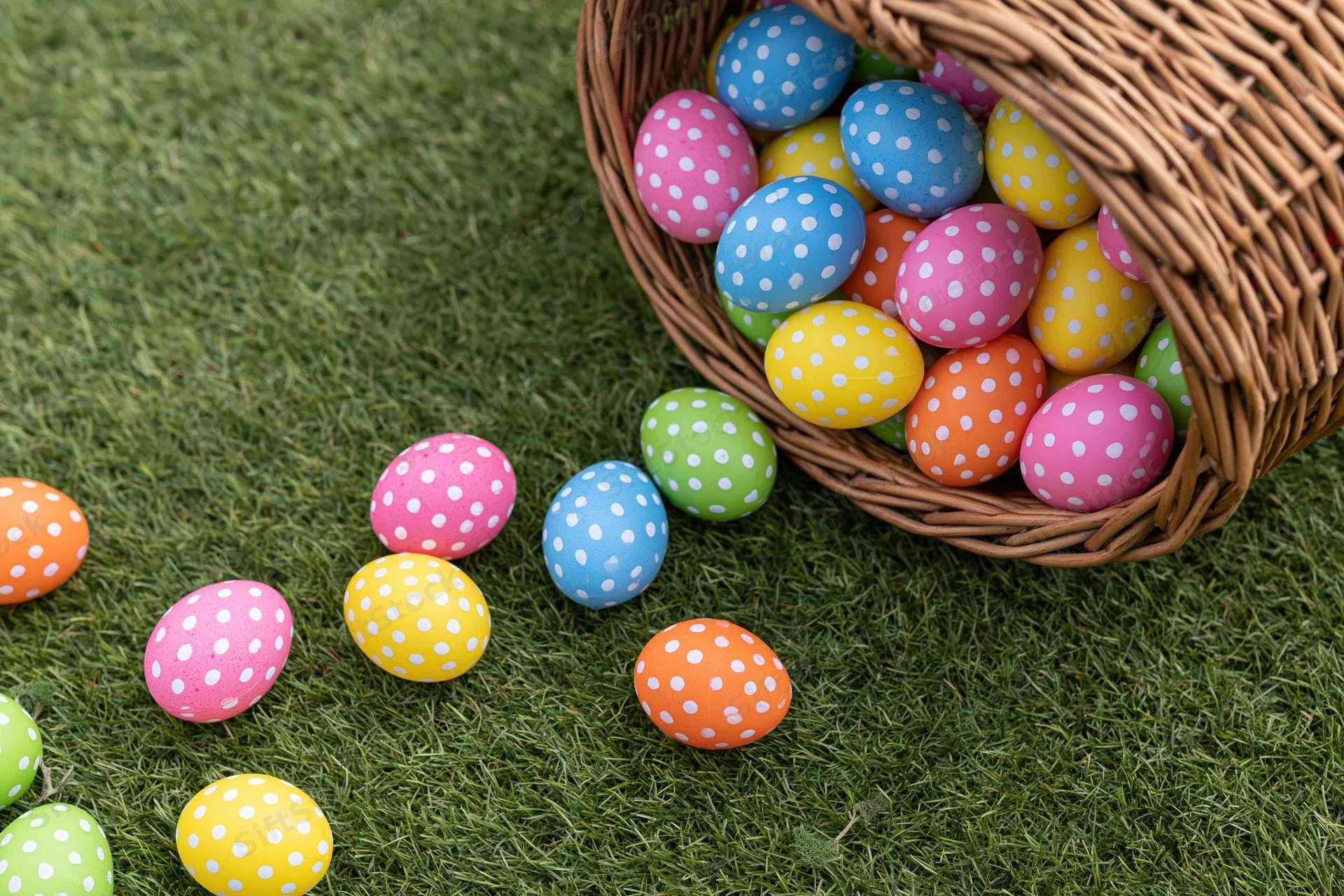 Wicker basket tipped over with colorful polka-dotted easter eggs scattered on green grass