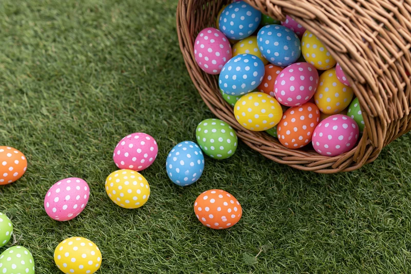Wicker basket tipped over with colorful polka-dotted easter eggs scattered on green grass