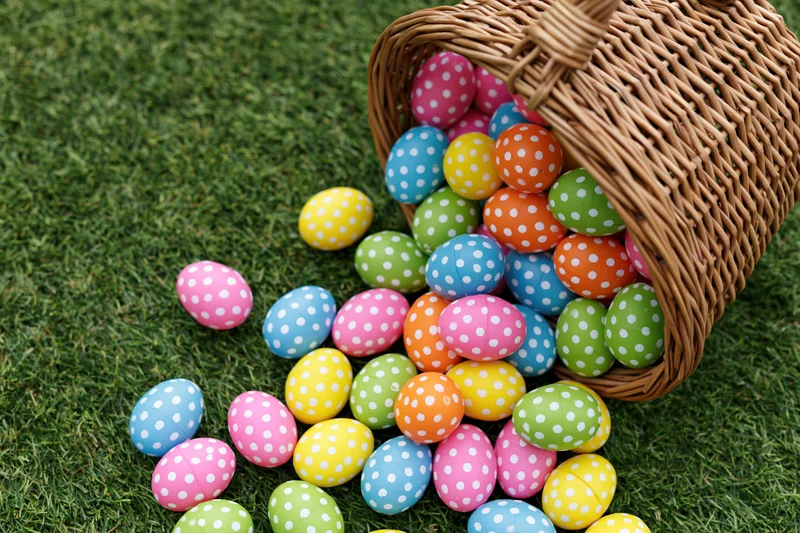 Wicker basket tipped over spilling colorful polka-dotted easter eggs onto green grass