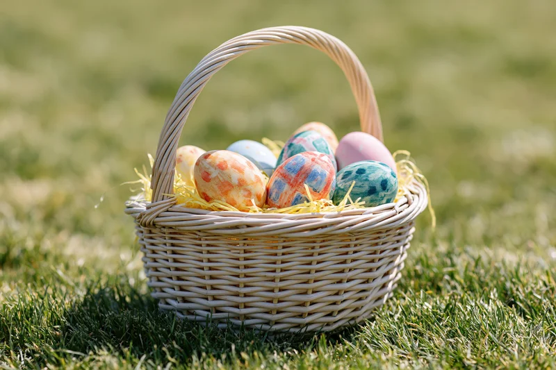 Wicker basket filled with hand-painted easter eggs on grass
