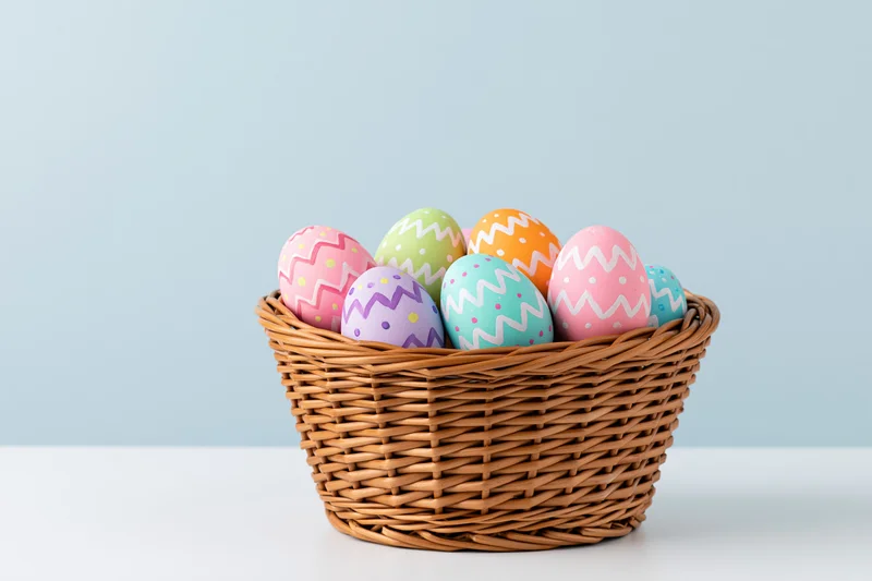 Wicker basket filled with painted easter eggs in pastel colors on a white surface against a light blue background