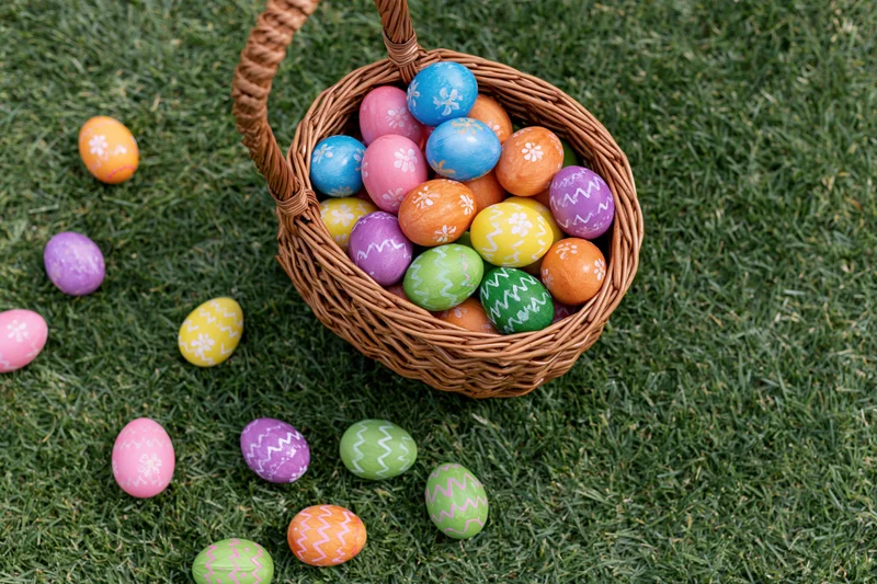 Wicker basket overflowing with hand-painted easter eggs scattered on green grass