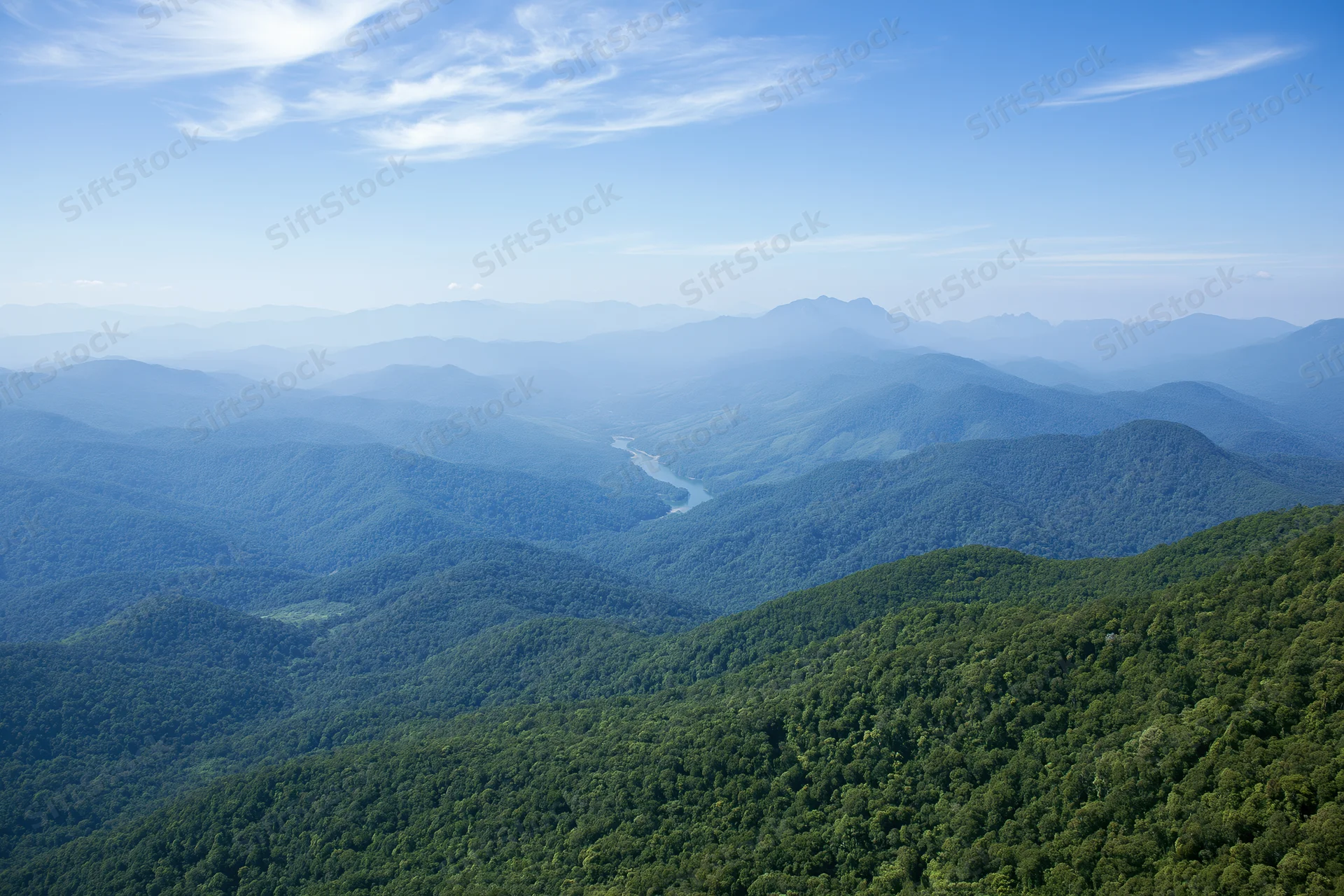 Aerial view of rolling forested hills and a winding river in a mountain valley
