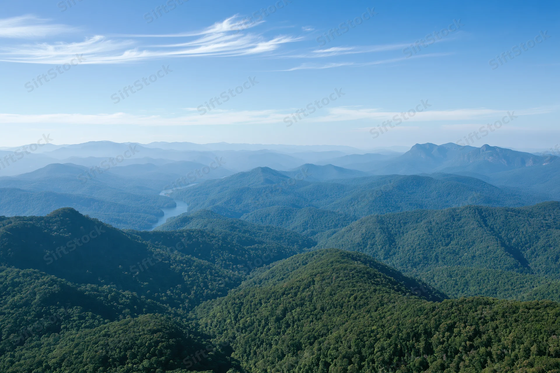 Aerial view of rolling forested hills receding into the distance under a clear blue sky