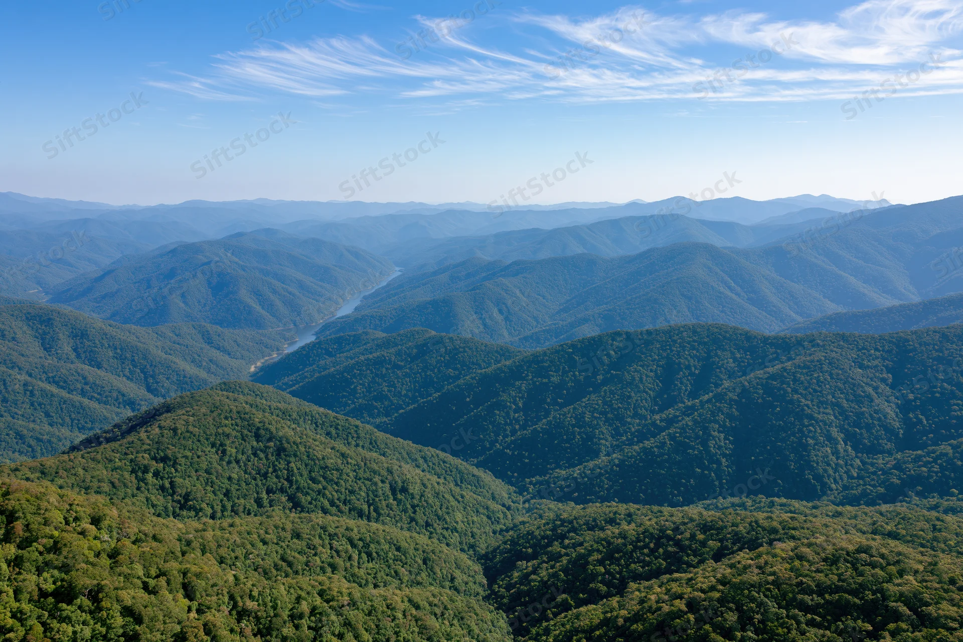 Aerial view of rolling forested hills and valleys receding into the distance under a blue sky with wispy clouds