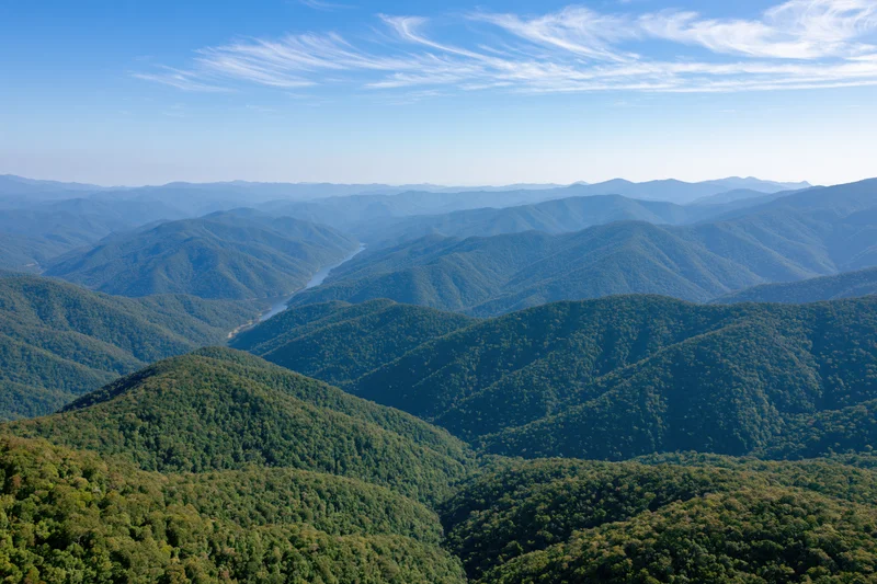 Aerial view of rolling forested hills and valleys receding into the distance under a blue sky with wispy clouds