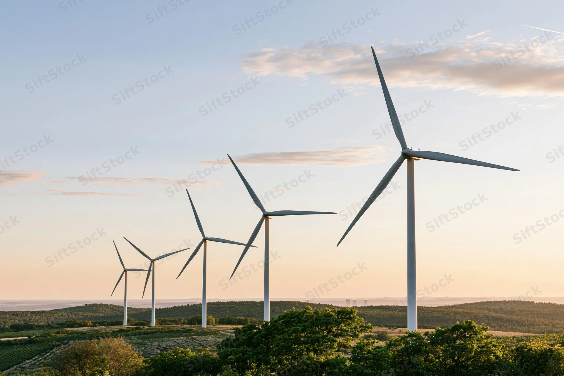 Wind turbines lined across a rolling green rural landscape at sunset