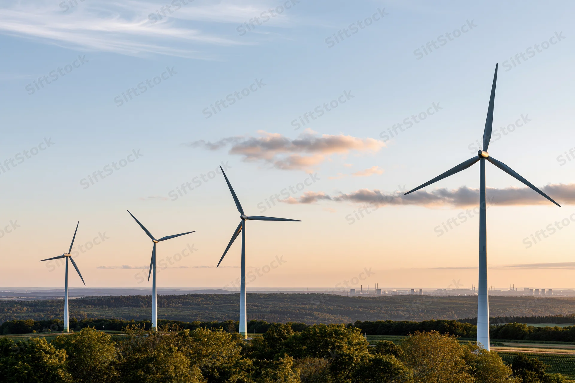 Wind turbines standing in a row across a rolling green rural landscape at sunset
