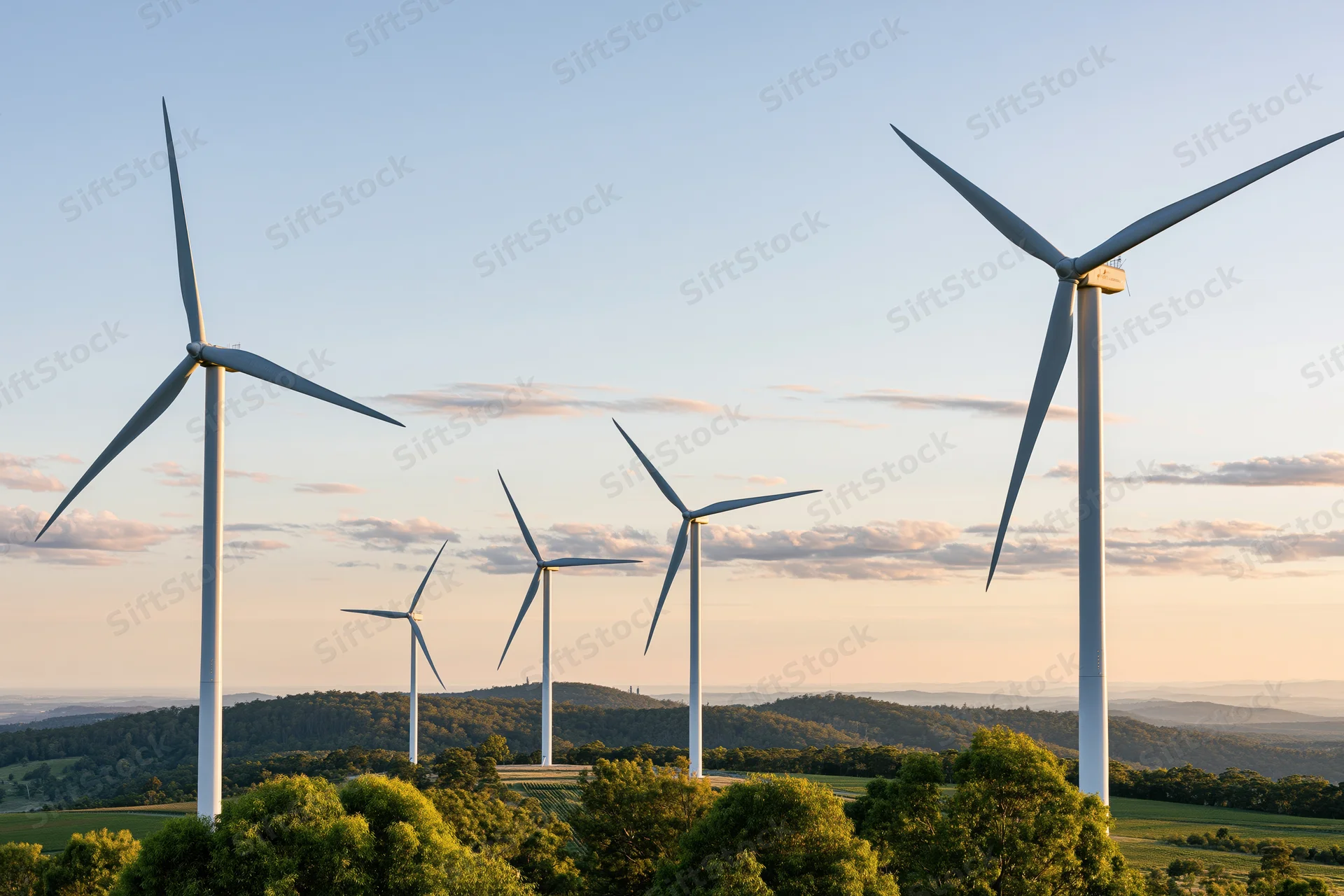 Wind turbines standing across a rolling green rural landscape at sunset