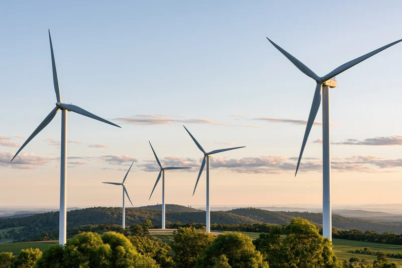 Wind turbines standing across a rolling green rural landscape at sunset