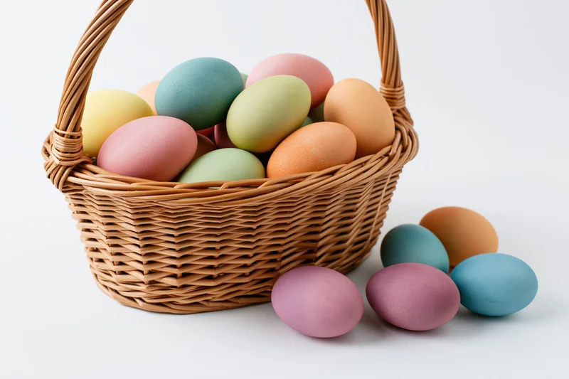 Wicker basket filled with pastel dyed easter eggs on white background