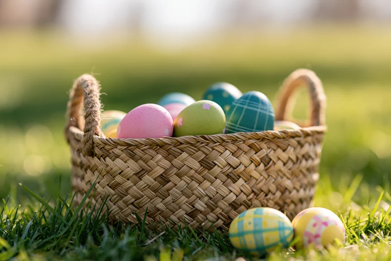 Woven straw basket filled with colorful painted easter eggs on green grass