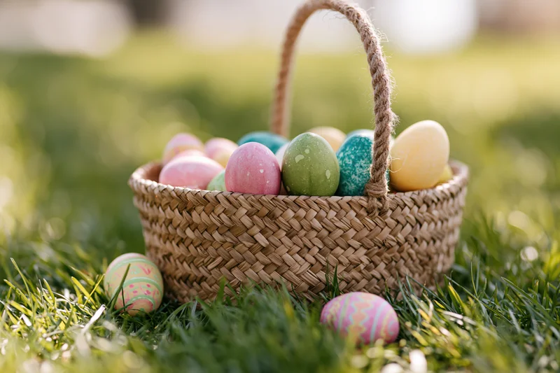 Woven straw basket filled with colorful painted easter eggs on green grass