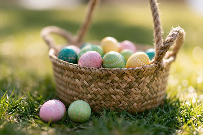 Woven straw basket filled with colorful painted easter eggs on green grass
