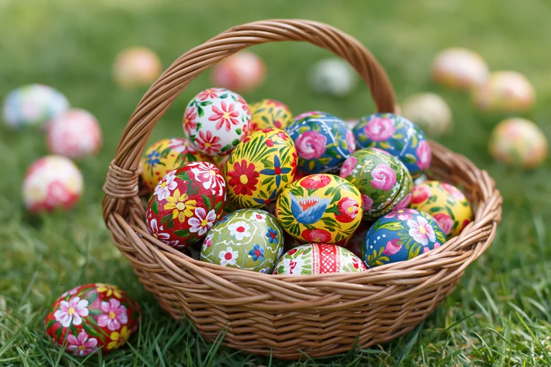 Woven wicker basket filled with hand-painted floral easter eggs on green grass