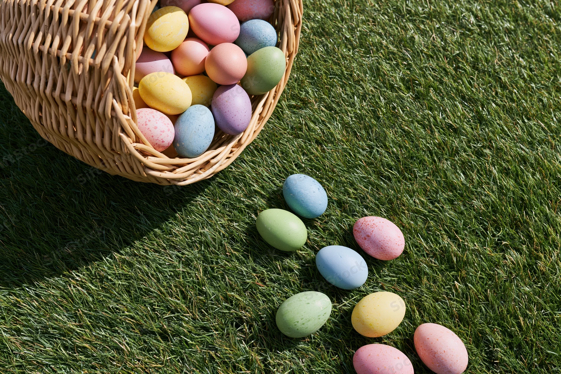 Tipped wicker basket spilling colorful dyed eggs onto green grass