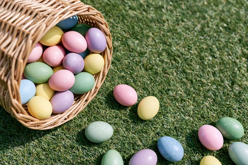 Tipped wicker basket spilling colorful easter eggs onto green grass