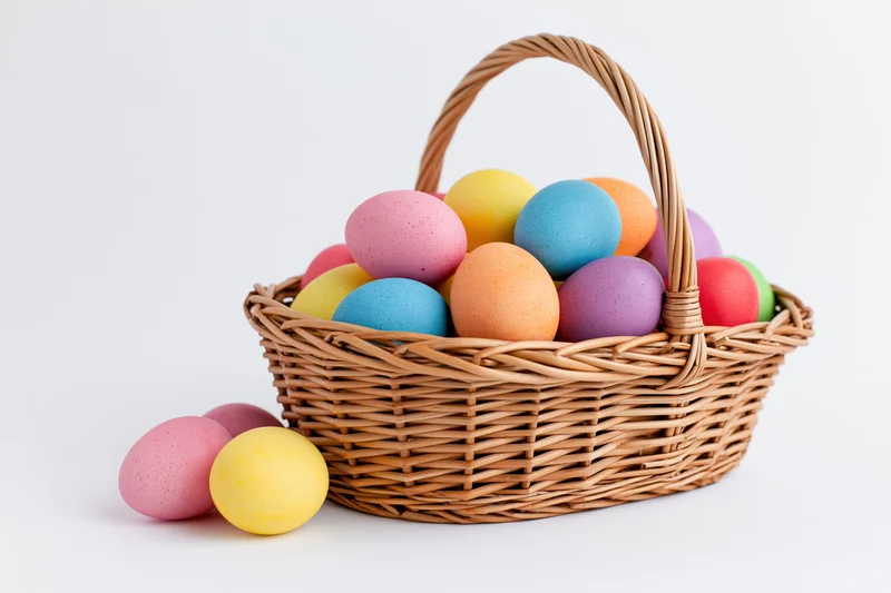 Woven wicker basket filled with colorful dyed eggs on white background