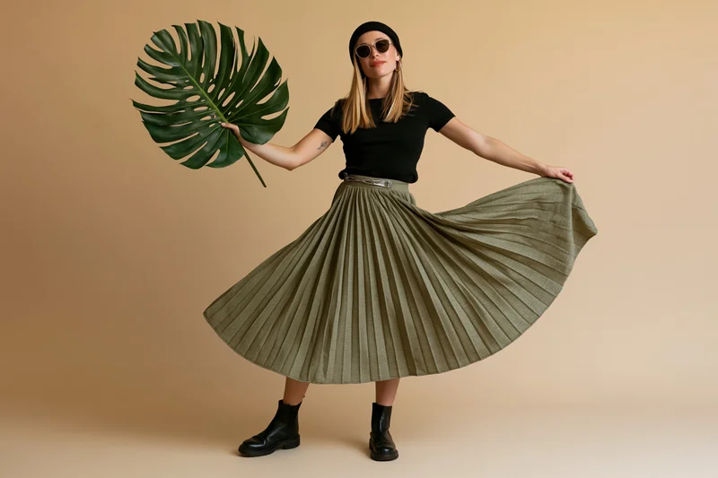 Young blonde woman spinning in pleated skirt holding large monstera leaf in studio