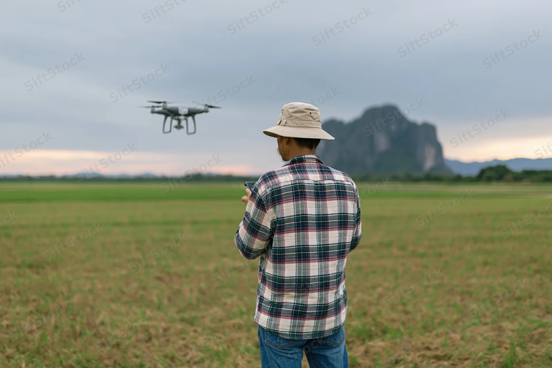 Farmer operating drone over crop field with mountain in background