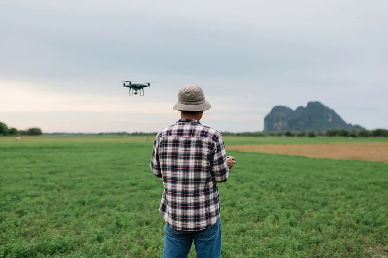 Farmer operating drone over green field with mountain in background
