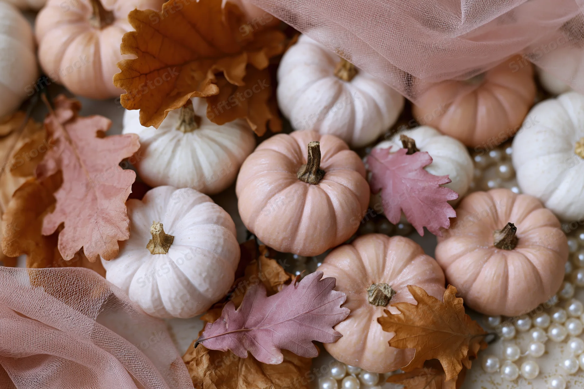 Small decorative pumpkins and autumn leaves arranged with pearls and tulle on a flat surface