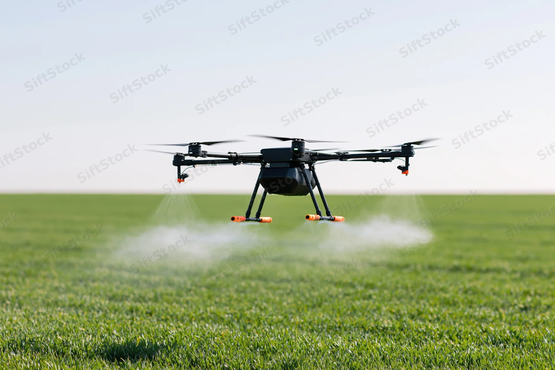 Black agricultural drone hovering over green field spraying liquid mist