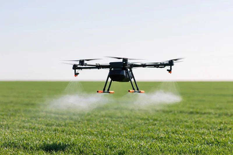 Black agricultural drone hovering over green field spraying liquid mist