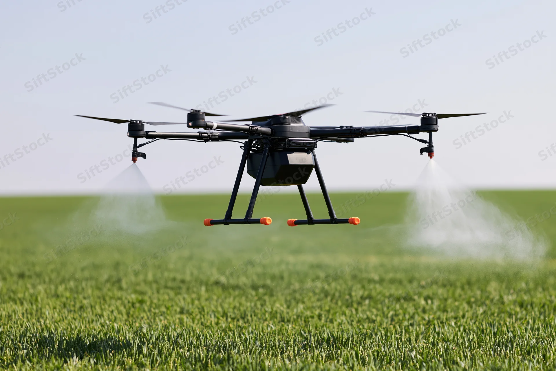 Black agricultural drone hovering over green field spraying liquid mist