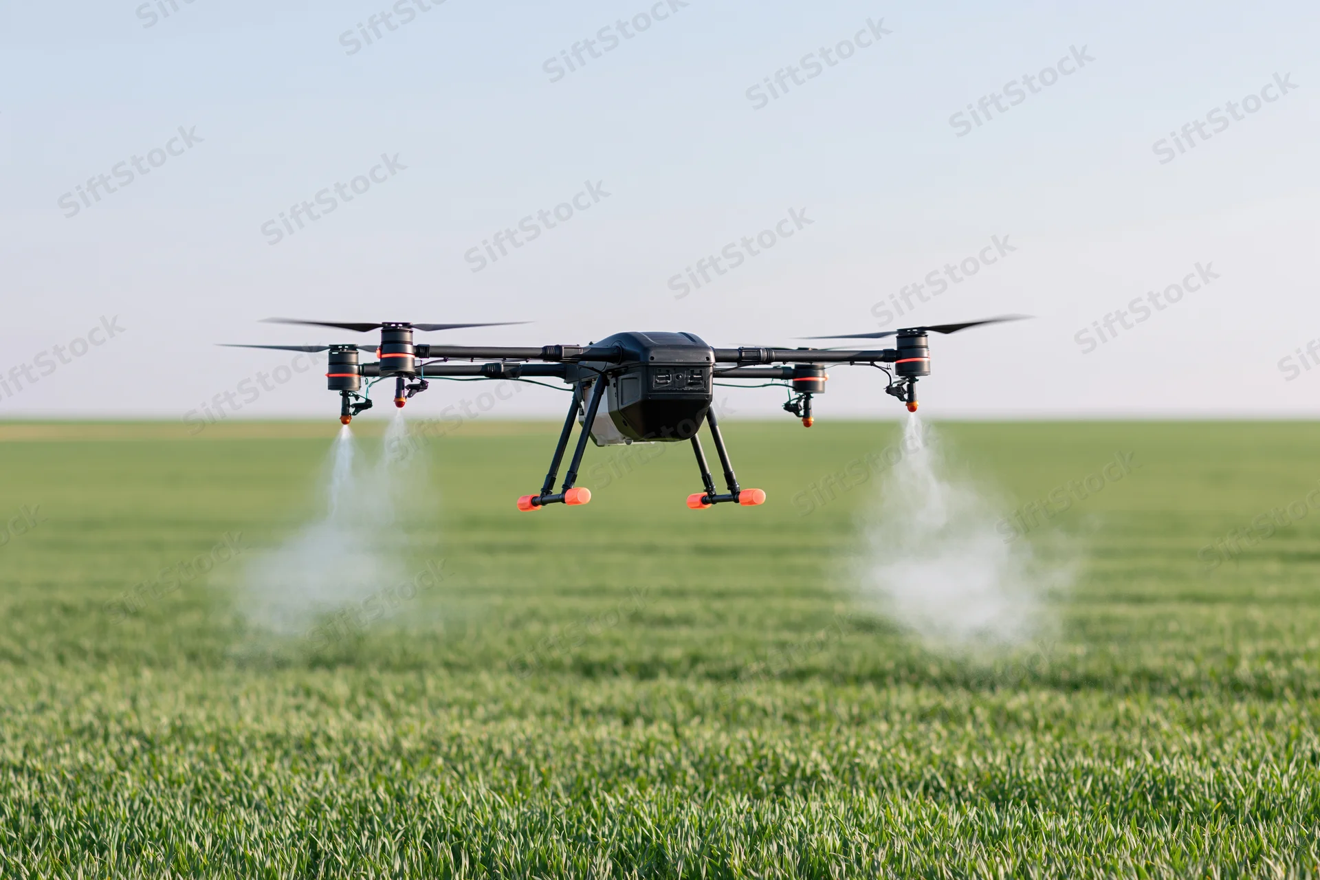 Black agricultural drone spraying liquid mist over green crop field during daytime
