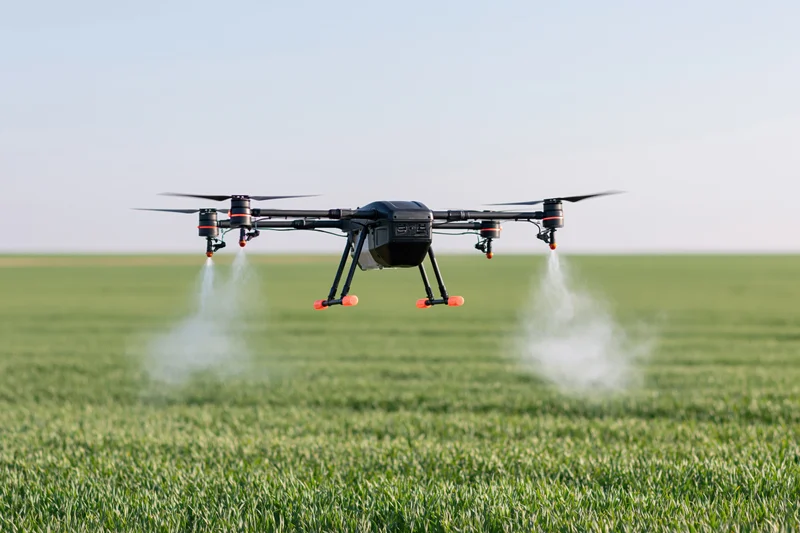 Black agricultural drone spraying liquid mist over green crop field during daytime
