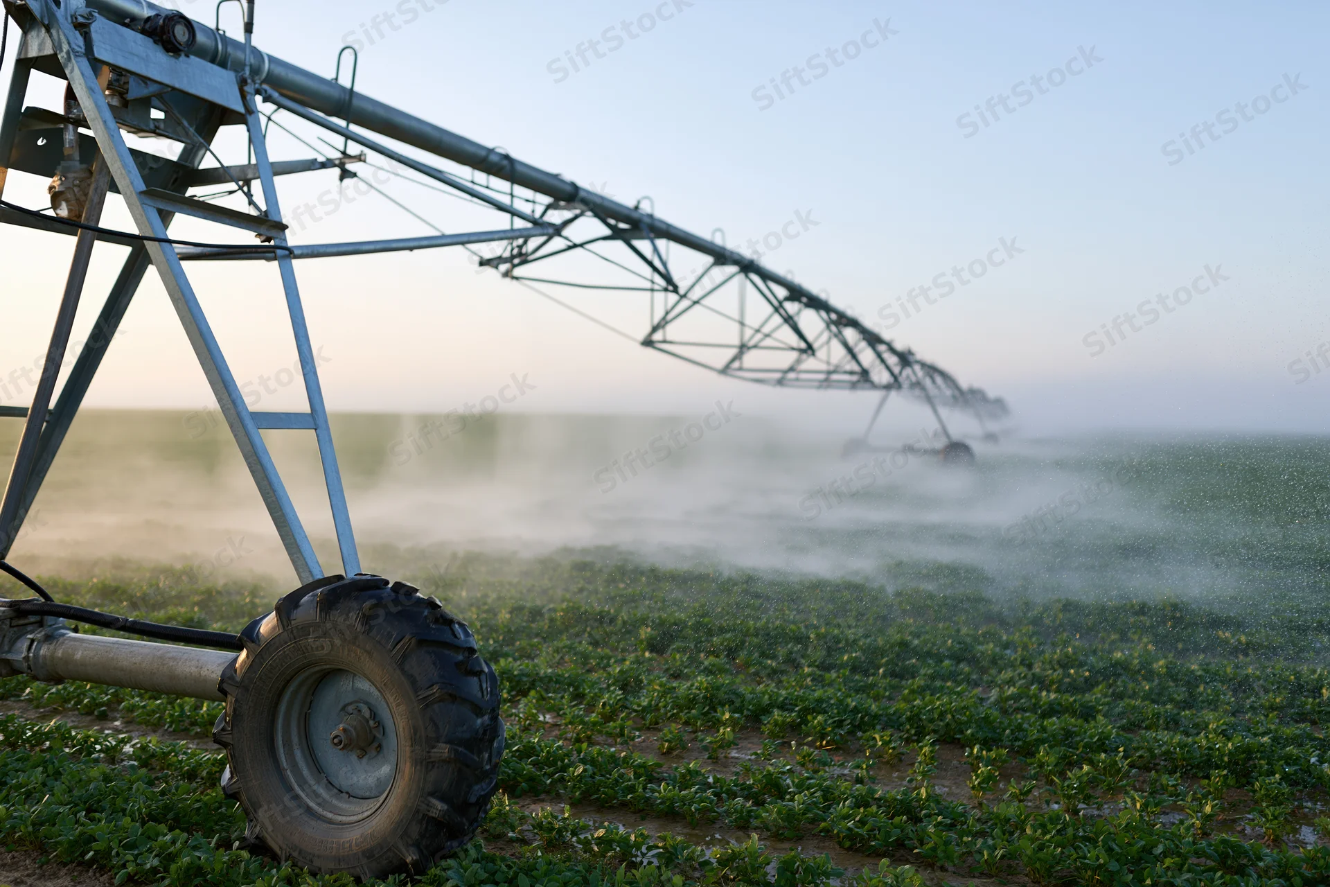 Center-pivot irrigation system spraying water across a green crop field in the daytime